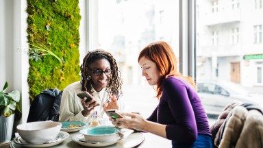 Foto de dos mujeres hablando por smartphone en una cafetería