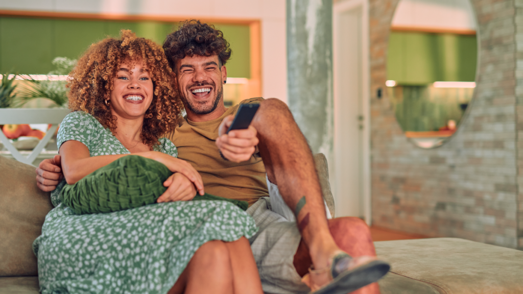 A couple laughing and watching TV  whose data will be collected via Nielsen's tv audience measurement solution.